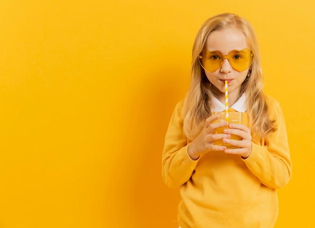 Free photo front view of girl posing while drinking juice and wearing sunglasses