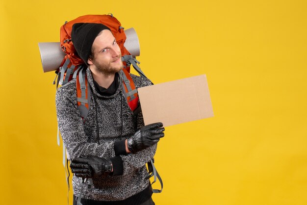 Free photo front view of glad young hitchhiker with leather gloves and backpack holding blank cardboard