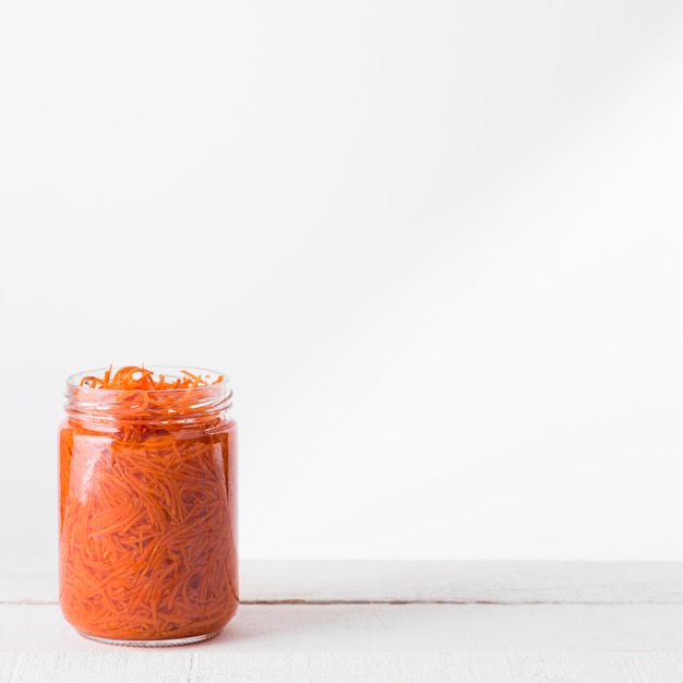 Front view of glass jar with preserved chopped baby carrots and copy space