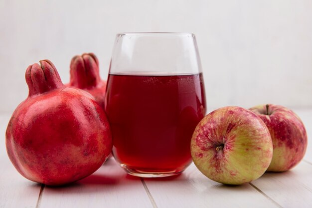 Front view glass of pomegranate juice with apples and pomegranates on white wall