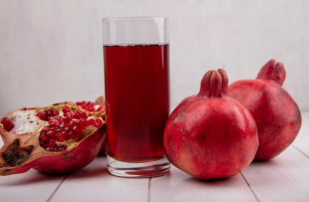 Front view glass of pomegranate juice with pomegranates on white wall