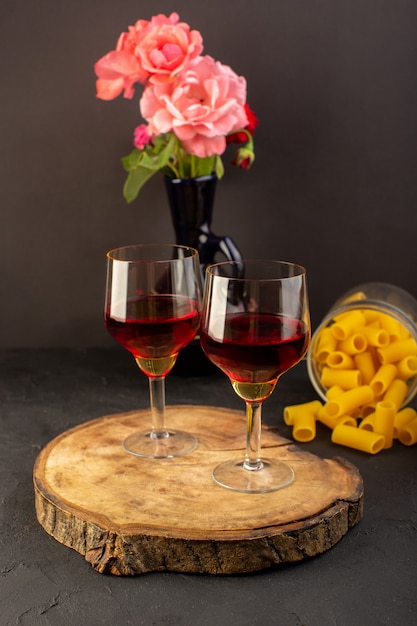 Free photo a front view glasses of wine on brown wooden desk along with flower and raw italian pasta on dark