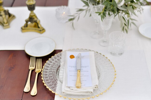 Front view of glassware and golden cutlery served on the wooden table and printed guest nameplate and white fabric serviettes