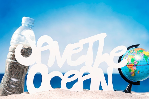 Front view of globe and plastic bottle with sand on beach