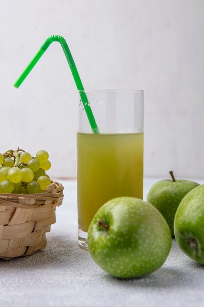 Front view green grapes in a basket with pear  green apples and apple juice with a green straw in a glass on a white background