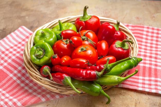 Front view green and red peppers hot peppers tomatoes in wicker basket and kitchen towel on amber background