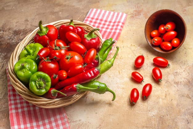 Front view green and red peppers hot peppers tomatoes in wicker basket scattered cherry tomatoes from bowl kitchen towel on amber background