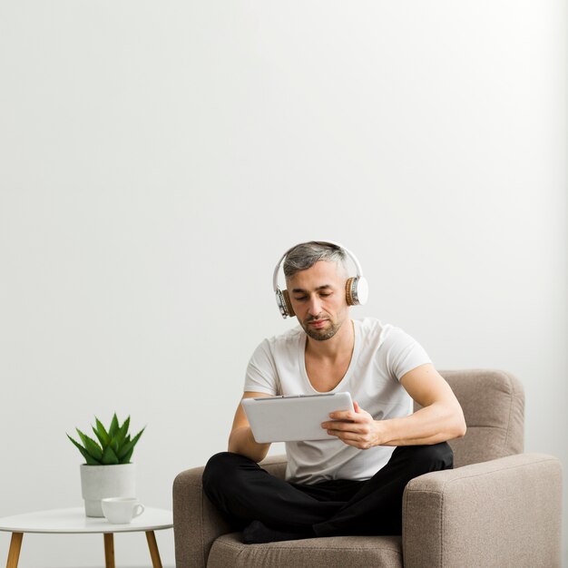 Front view guy with headphones looking at his tablet