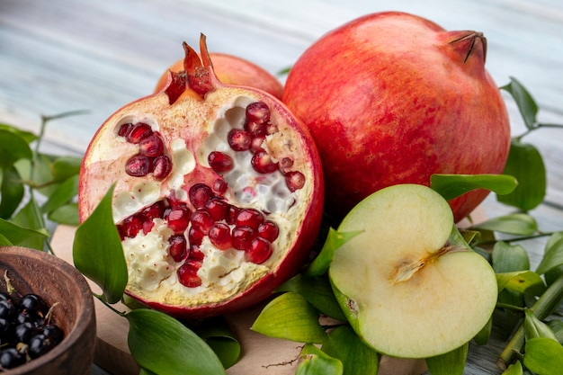 Front view of half pomegranate with a branch of leaves and an apple on a gray surface