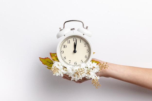 Front view of hand holding clock with flowers