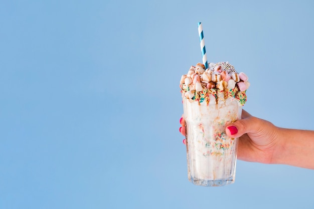 Free photo front view of hand holding milkshake with blue background