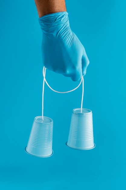 Front view of hand with glove holding plastic cups with string