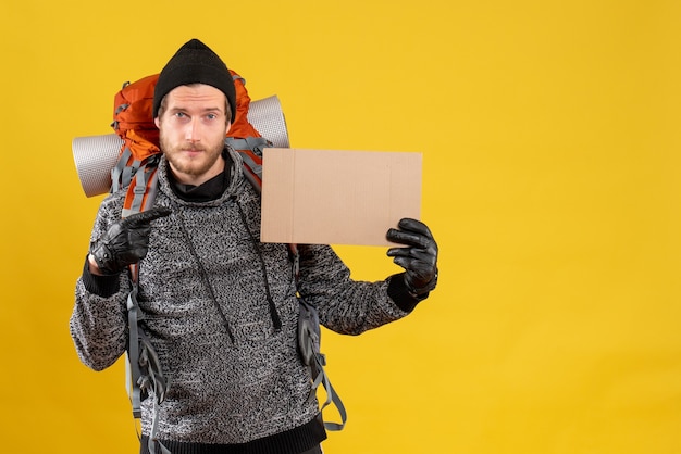 Free photo front view of handsome hitchhiker with leather gloves and backpack pointing at blank cardboard