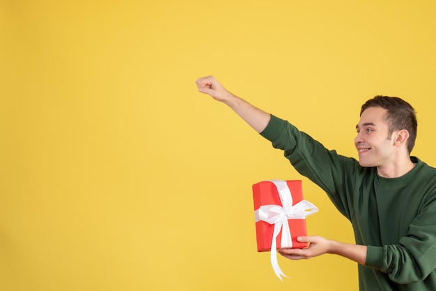 Free Photo front view handsome young man holding gift aking super hero gesture on yellow 