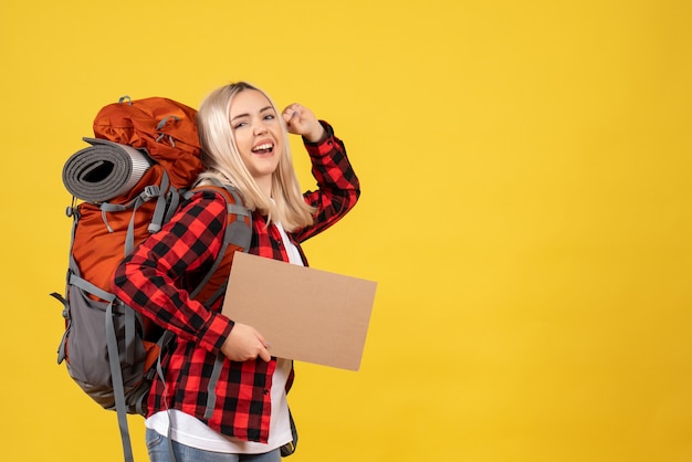 Front view happy blonde woman with her backpack holding up cardboard