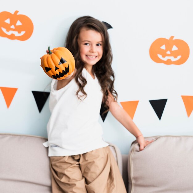 Front view happy little girl holding a pumpkin