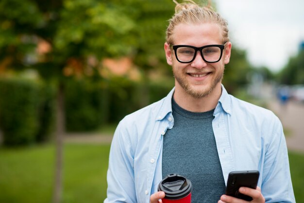 Front view of happy man outdoors with smartphone and cup