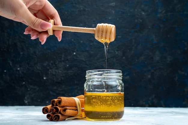 Free photo a front view honey and cinnamon female dunking spoon into the honey on the blue-grey background sugar  plant