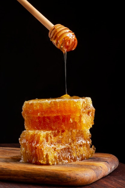 Front view of honey dipper dripping honey on honeycomb