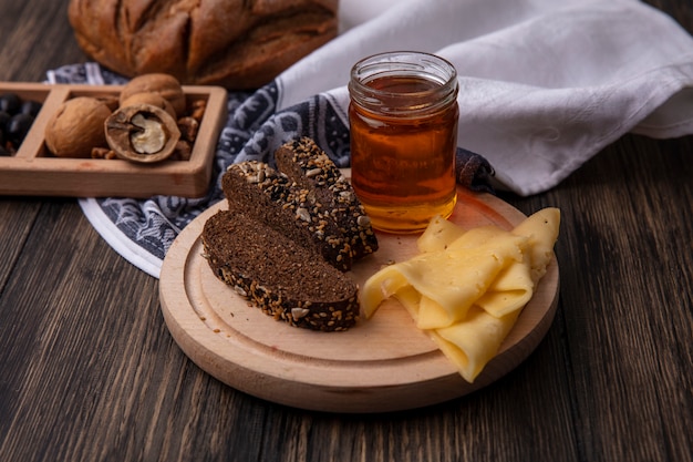 Front view honey in a jar with black bread and cheese on a stand with walnuts on a wooden background