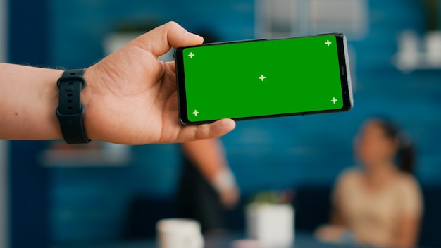 Free photo front view of horizontal isolated mock up green screen chroma key display of modern phone. two collegues talking about internet browsing and social media in home studio background