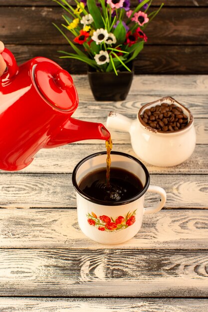 Front view of hot cup pouring from red kettle brown coffee seeds and flowers on the wooden desk