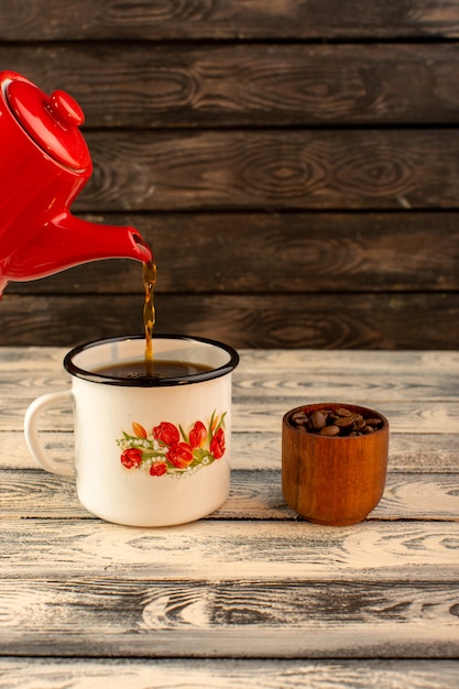 Front view of hot tea pouring from red kettle on the wooden desk