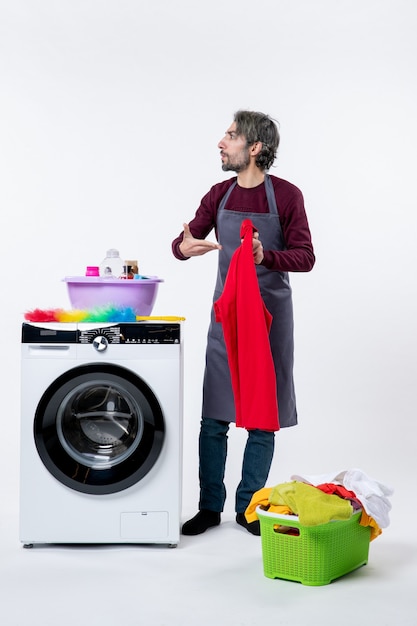 Front view housekeeper man pointing at red towel standing near washing machine on white background