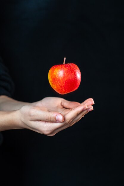 Front view of human hands with an apple on dark surface