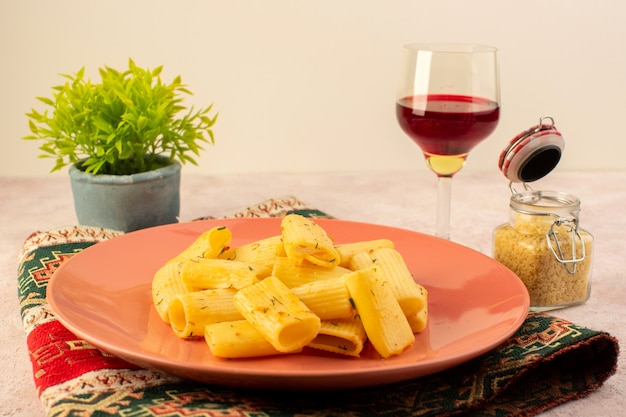 A front view italian pasta tasty meal inside pink plate along with raw pasta and glass of wine on colorful carpet and pink