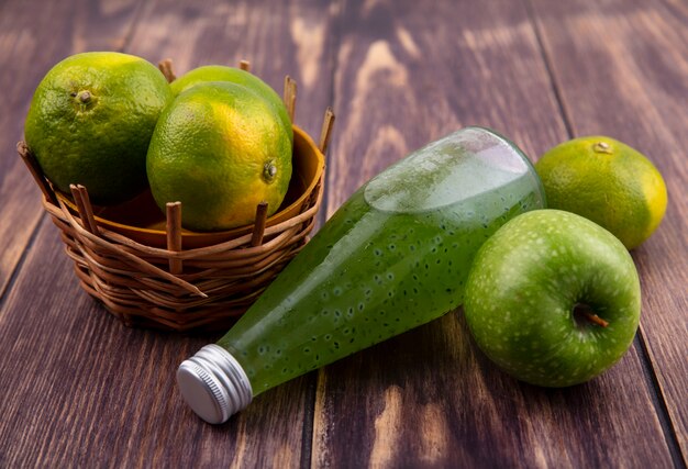 Front view juice bottle with tangerines in basket and apple on wooden wall