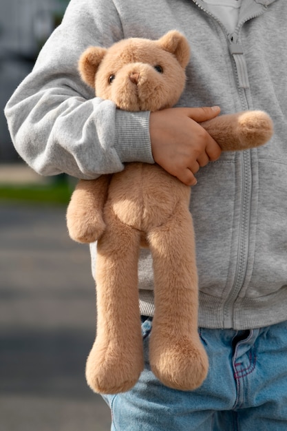 Free photo front view kid holding teddy bear outdoors