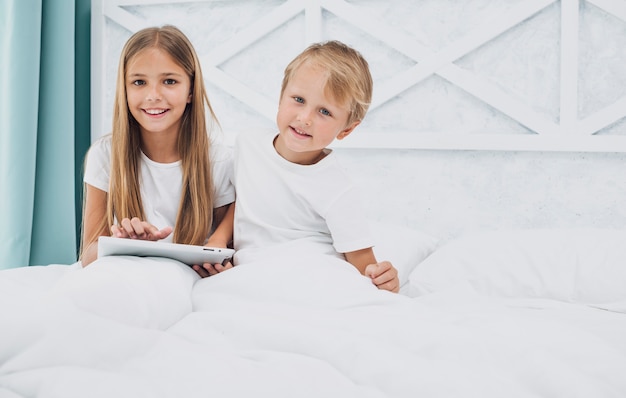 Front view kids staying in bed while playing on a tablet