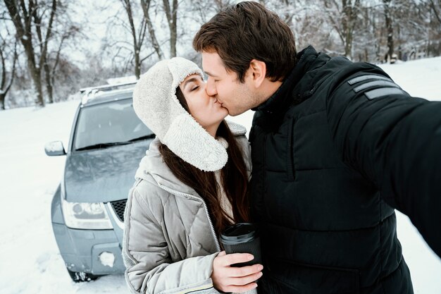 Front view of kissing couple taking selfie while on a road trip