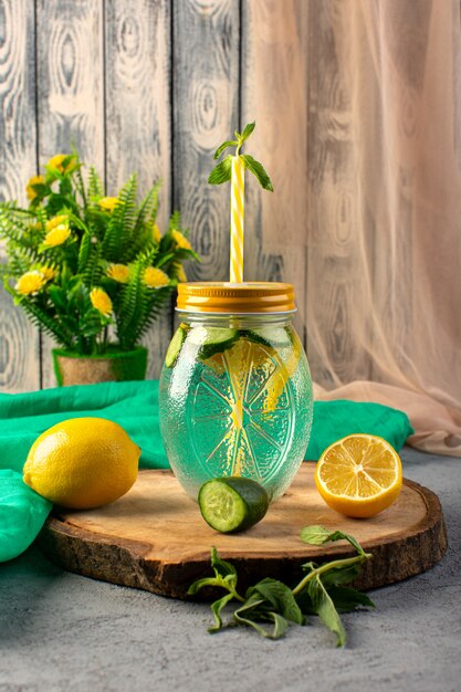 Free photo a front view lemon cocktail fresh cool drink inside glass cup sliced lemons flowers straw on the wooden desk and grey background cocktail drink fruit