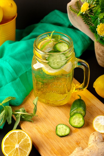 Free Photo a front view lemon cocktail fresh cool drink inside glass cup sliced and whole lemons cucumbers along with flowers on the dark background cocktail drink fruit