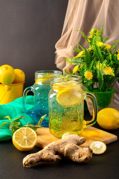 A front view lemon cocktail fresh cool drink inside glass cups sliced and whole lemons along with flowers on the dark background cocktail drink fruit