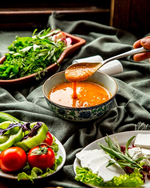 Front view lentil soup traditional azerbaijani soup with a spoon over a plate in hand and with greens vegetables and cheese on the table