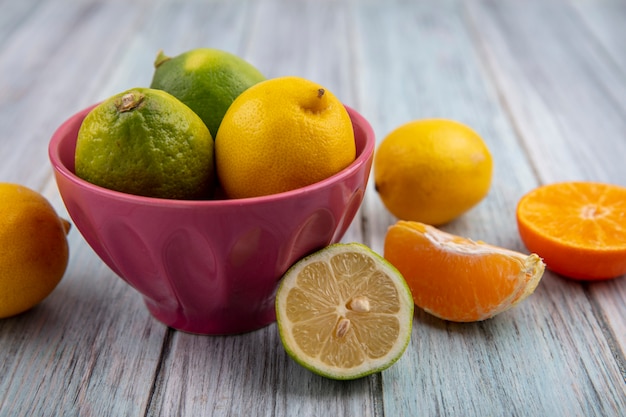 Front view limes with lemons in a bowl and orange slices on gray background