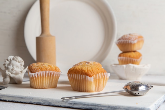 Front view of little cakes inside paper forms with sugar powder on the white desk