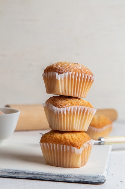 Front view of little cakes inside paper forms with sugar powder on the white surface