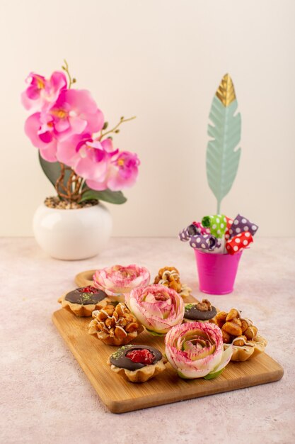 A front view little chocolate cakes with flower on the pink desk