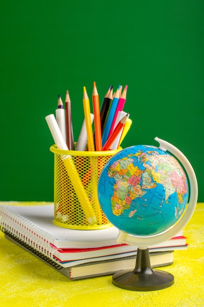 Free photo front view little globe with copybooks and pencils on yellow surface