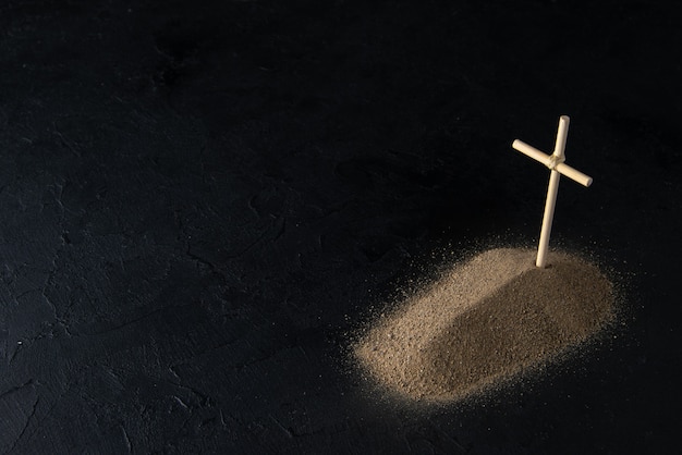 Front view of little grave from sand with stick cross on black