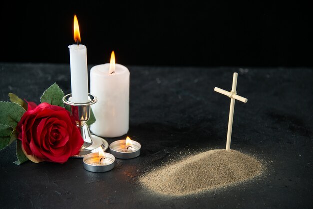 Front view of little grave with red rose and candles on black