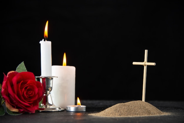 Front view of little grave with red rose and candles on black