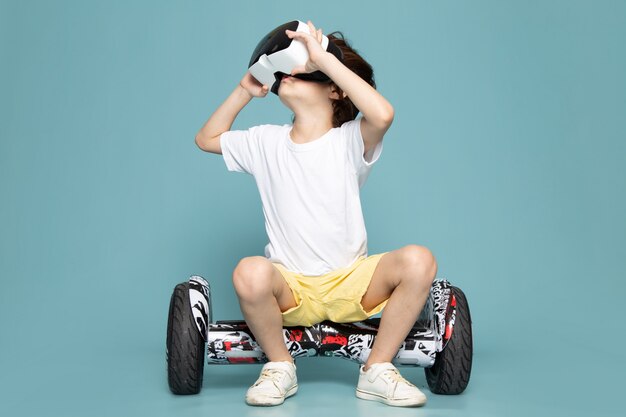 A front view little smiling boy playing vr on segway on the blue floor