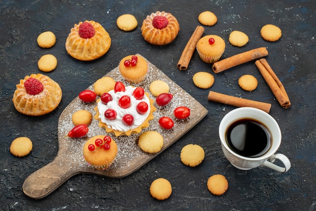 Front view little yummy cakes with cream cinnamon coffee and fresh fruits on the dark surface sweet biscuits cake dessert fruit berry