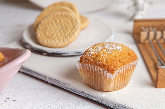 Front view of little yummy cakes with sugar powder and cookies on the white desk