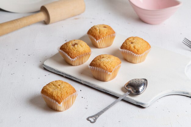 Front view of little yummy cakes with sugar powder inside plate with spoon on the white surface